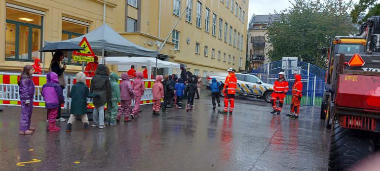 en gruppe mennesker som står på en gate med en brannbil og en bygning i bakgrunnen
